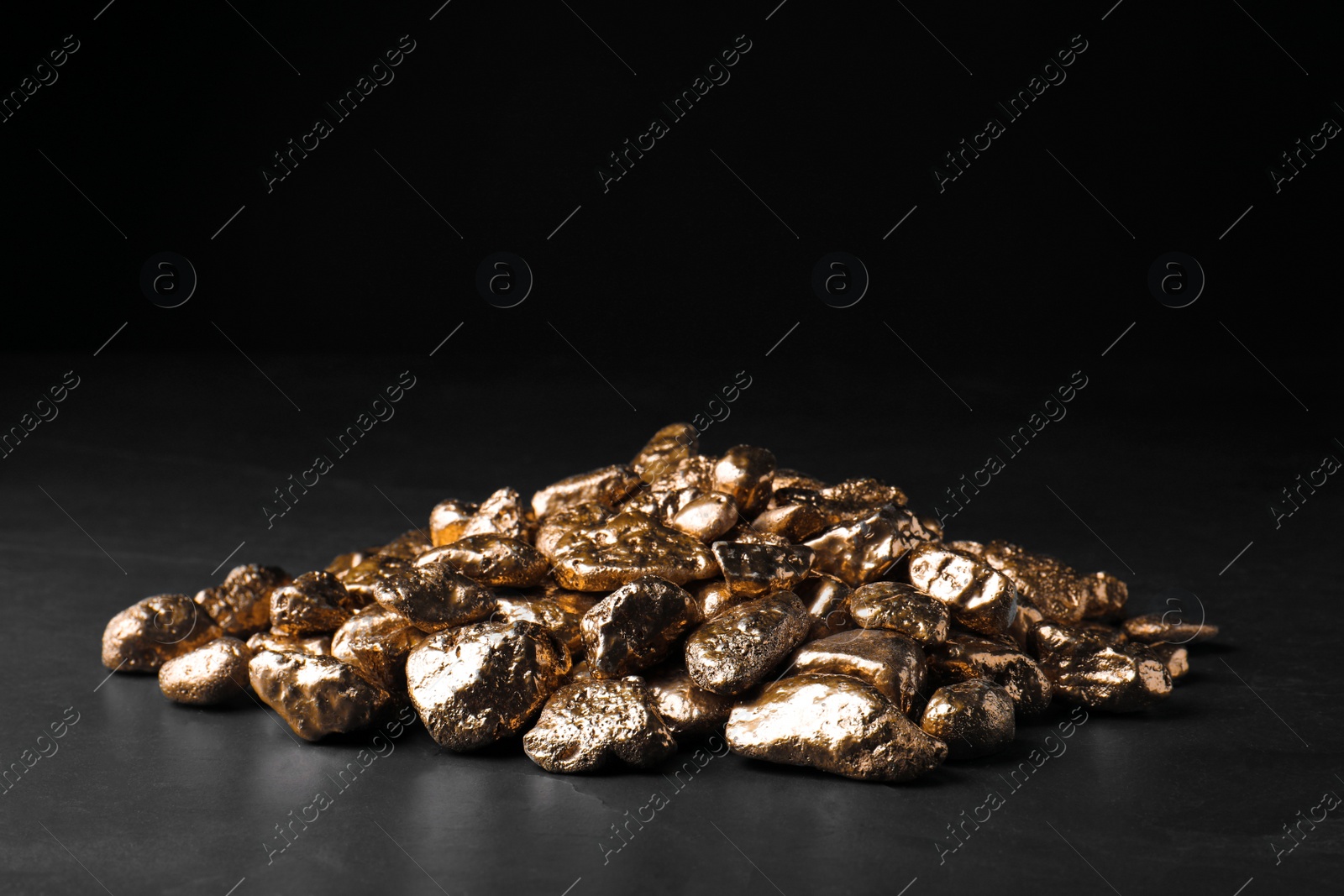 Photo of Pile of gold nuggets on black table against dark background, space for text