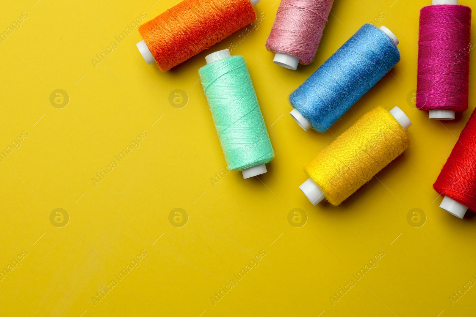 Photo of Different colorful sewing threads on yellow background, flat lay. Space for text