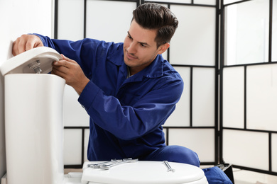 Professional plumber working with toilet bowl in bathroom