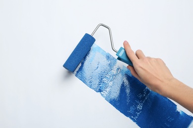 Woman painting with roller brush on white background, closeup view