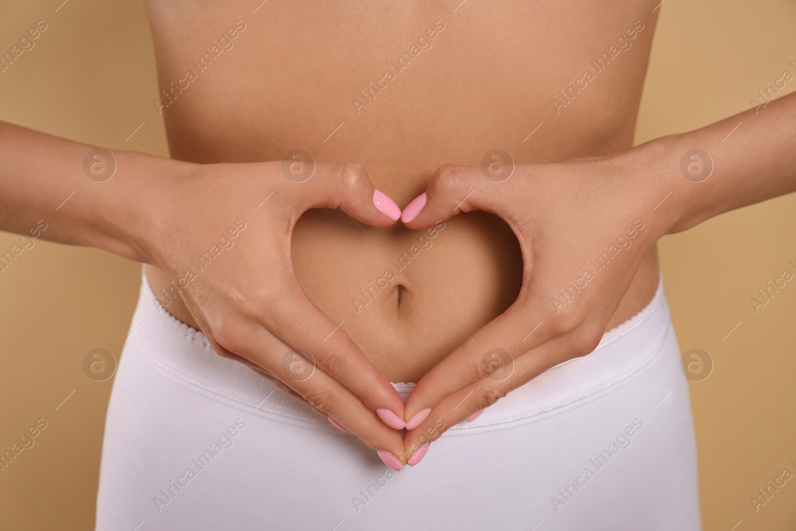 Photo of Woman in underwear making heart with hands on her belly against beige background, closeup. Healthy stomach