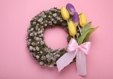 Wreath made of beautiful willow, colorful tulip flowers and bow on pink background, top view