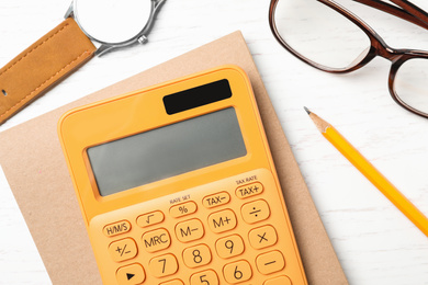 Calculator, notebook, watch and glasses on white wooden table, flat lay. Tax accounting