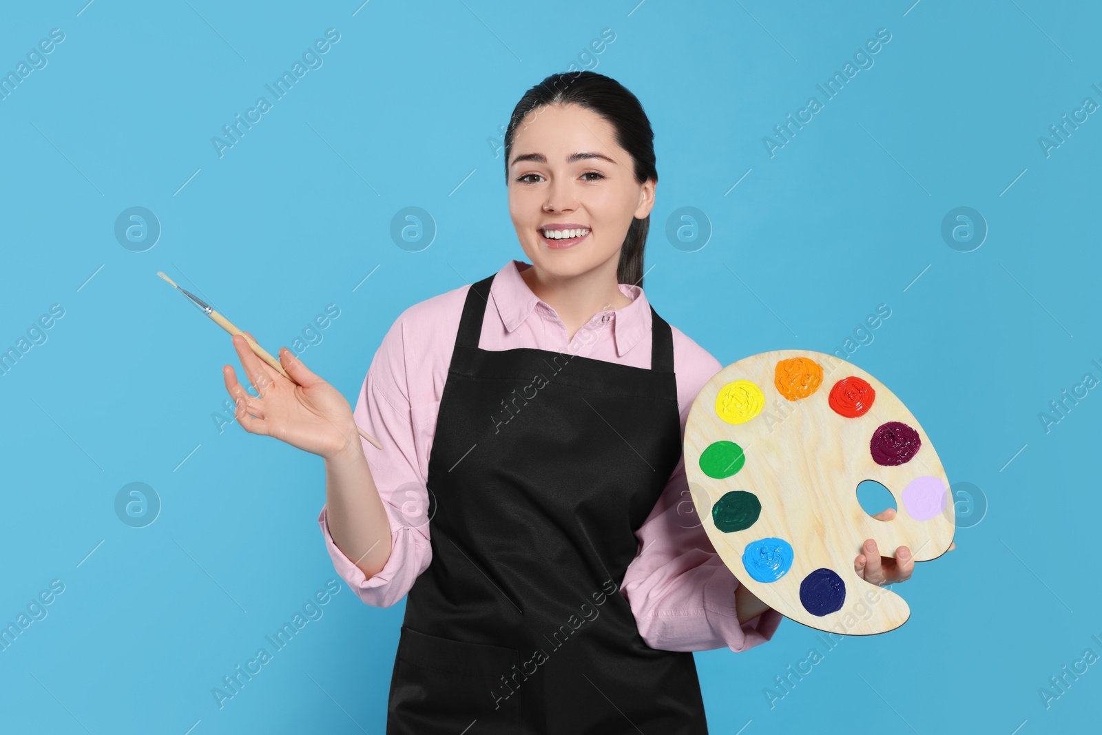 Photo of Woman with painting tools on light blue background. Young artist