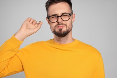 Young man cleaning ear with cotton swab on light grey background