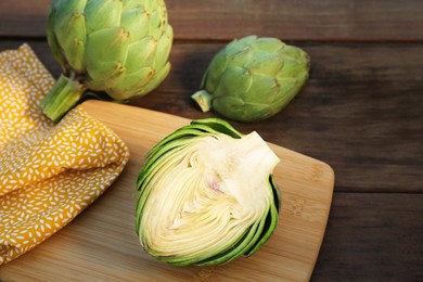 Photo of Whole and cut fresh raw artichokes on wooden table, closeup