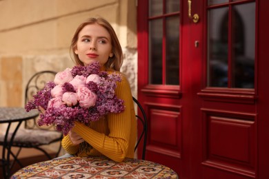 Photo of Beautiful woman with bouquet of spring flowers in outdoor cafe, space for text