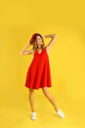 Beautiful young woman in red dress dancing on yellow background