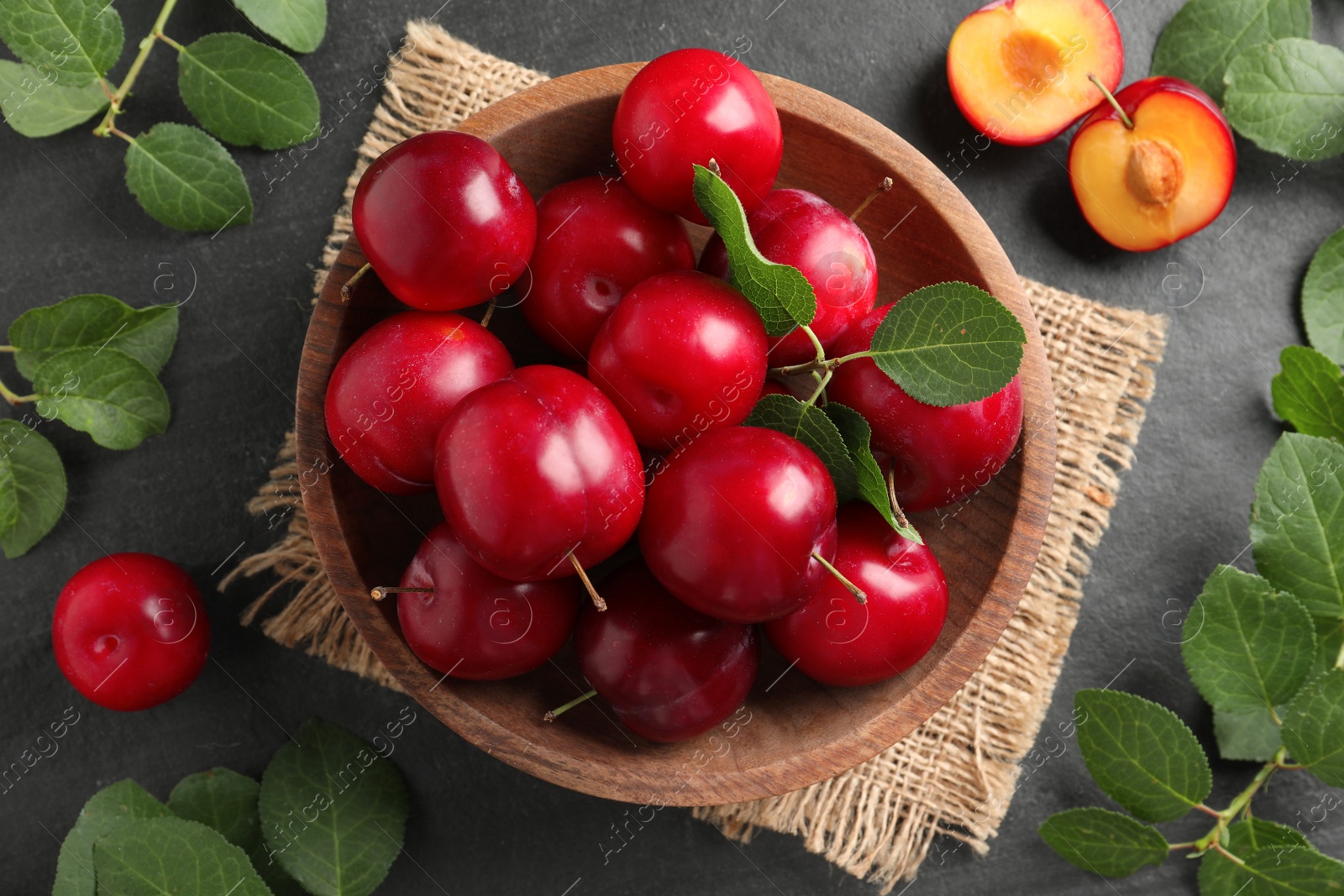 Photo of Delicious ripe cherry plums with leaves on black table, flat lay