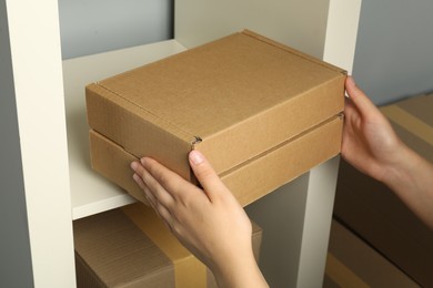 Photo of Woman putting cardboard box on shelf indoors, closeup. Packaging goods