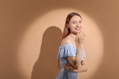Photo of Beautiful young woman in sunlight on beige background, space for text