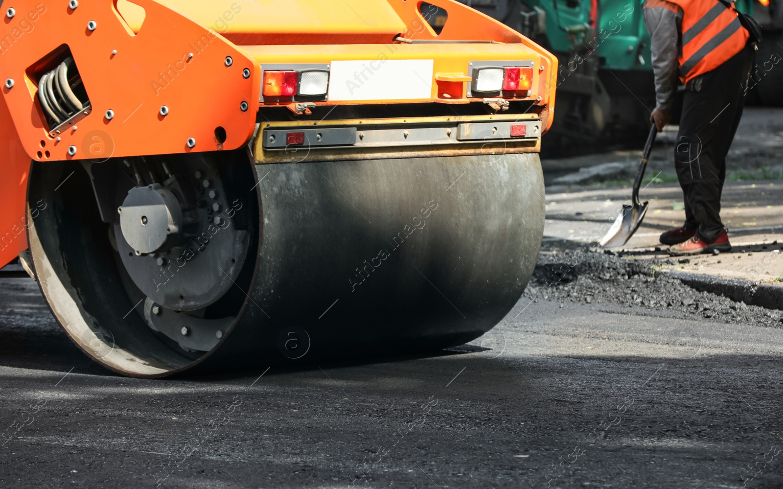Photo of MYKOLAIV, UKRAINE - AUGUST 05, 2021: Worker laying new asphalt with roller on city street. Road repair service