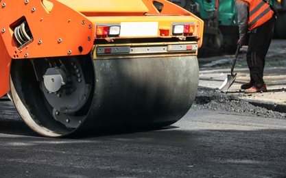 Photo of MYKOLAIV, UKRAINE - AUGUST 05, 2021: Worker laying new asphalt with roller on city street. Road repair service