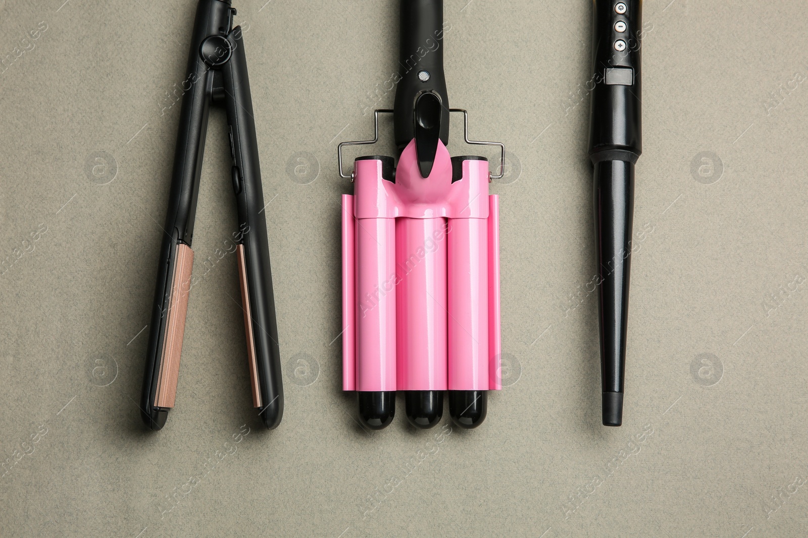 Photo of Set of modern hair irons on grey background, flat lay