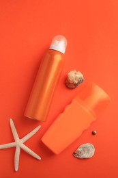 Bottles of sunscreen, seashells and starfish on coral background, flat lay