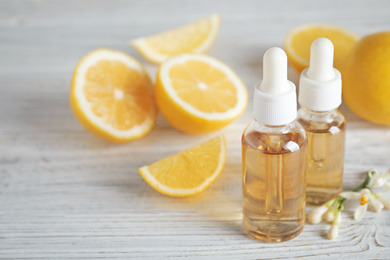 Bottles of citrus essential oil, flower and lemons on white wooden table. Space for text