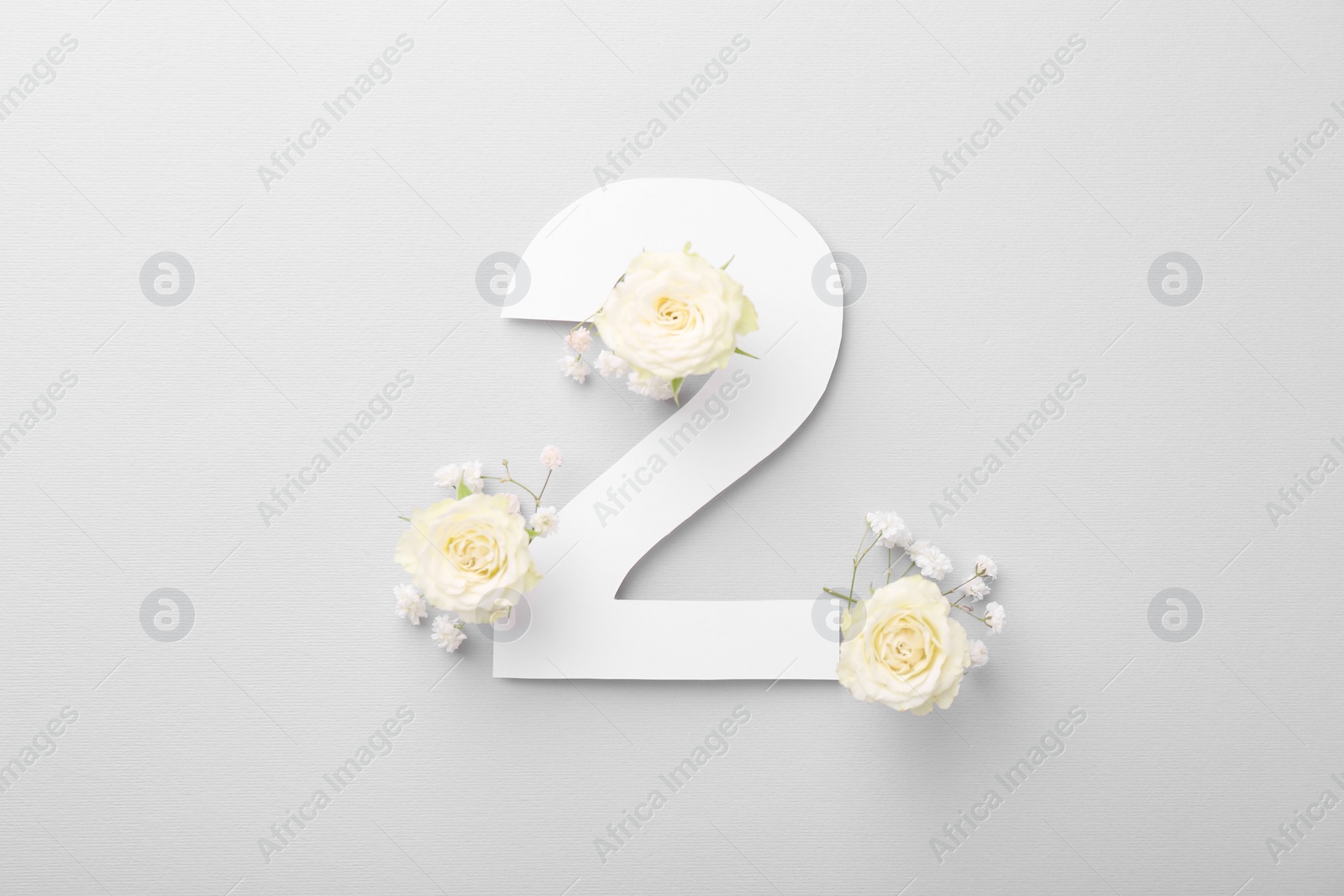 Photo of Paper number 2 and beautiful flowers on light grey background, top view