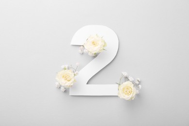 Photo of Paper number 2 and beautiful flowers on light grey background, top view