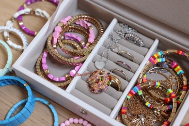 Photo of Jewelry box with stylish bracelets and other accessories on wooden table, above view