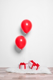 Red balloons and gifts on floor against white wall