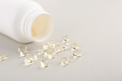 Photo of Vitamin capsules and bottle on light grey background, closeup. Space for text