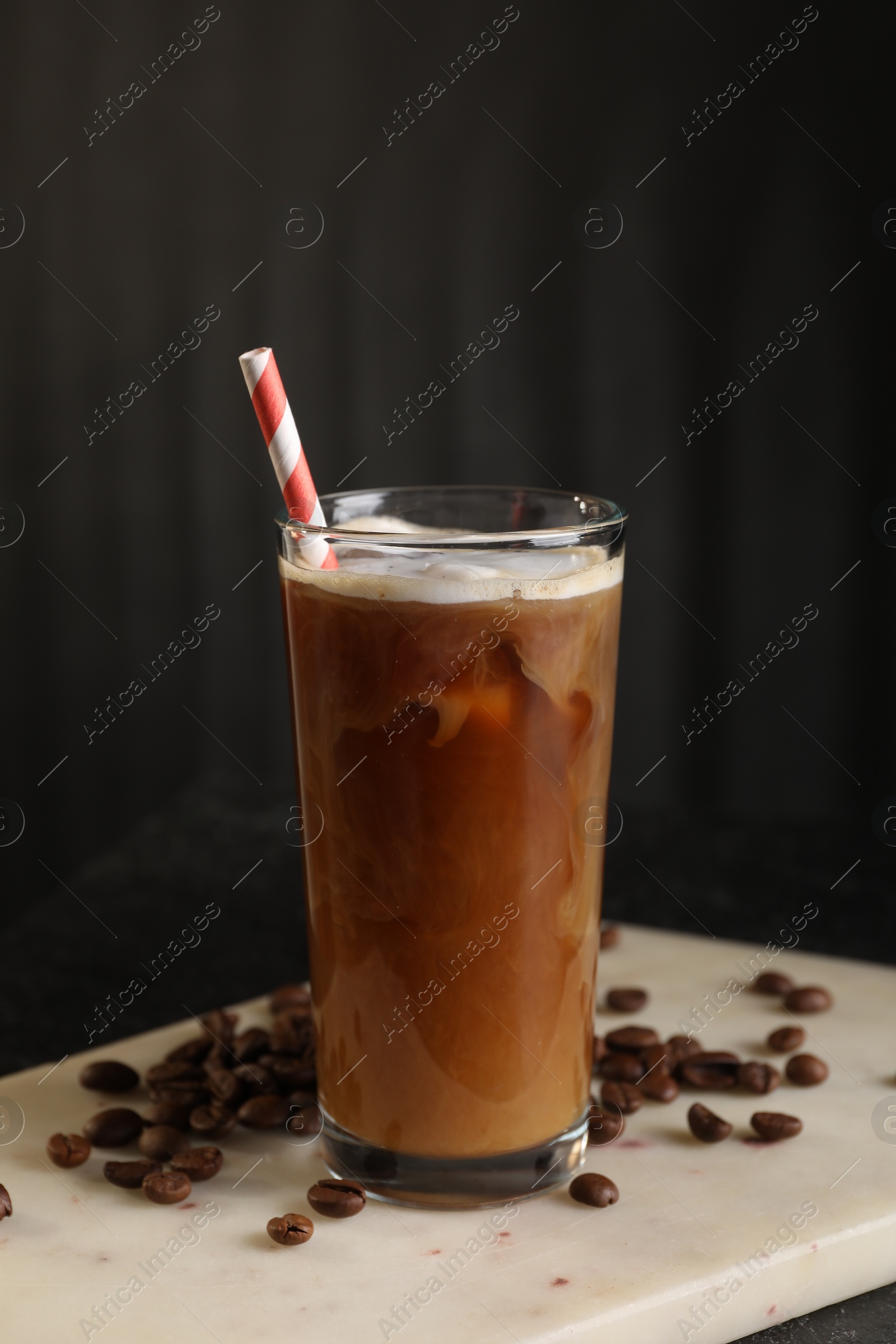 Photo of Refreshing iced coffee with milk in glass and beans on table against dark gray background
