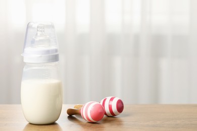 Feeding bottle with milk and toy maracas on wooden table indoors. Space for text