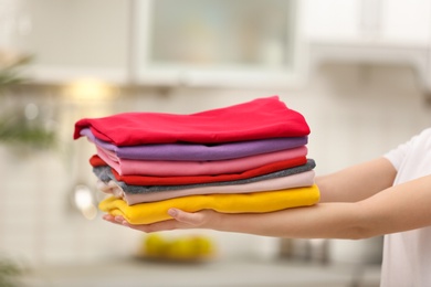 Photo of Woman holding folded clean clothes indoors, closeup. Laundry day