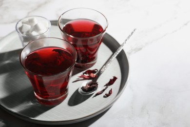 Photo of Delicious hibiscus tea, sugar cubes and dry roselle petals on white table. Space for text