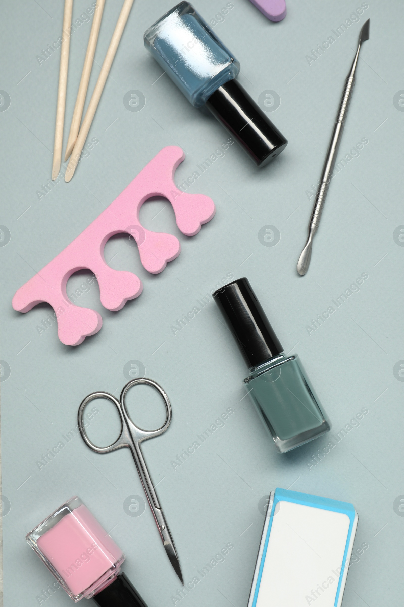 Photo of Nail polishes and set of pedicure tools on grey background, flat lay