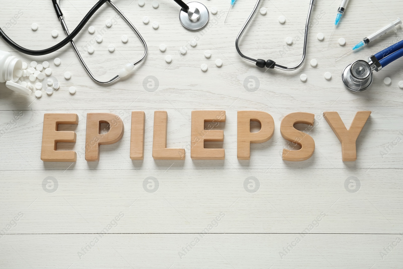Photo of Word Epilepsy made of wooden letters, stethoscopes, pills and syringes on white table, flat lay