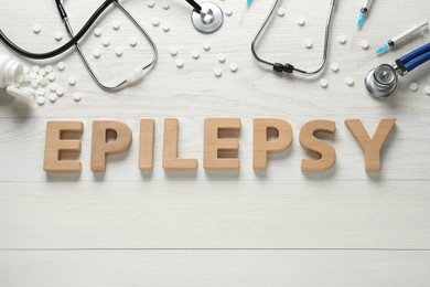 Photo of Word Epilepsy made of wooden letters, stethoscopes, pills and syringes on white table, flat lay