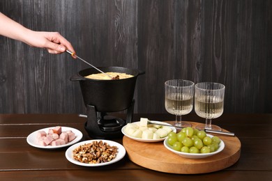Photo of Woman dipping walnut into fondue pot with tasty melted cheese at white wooden table, closeup