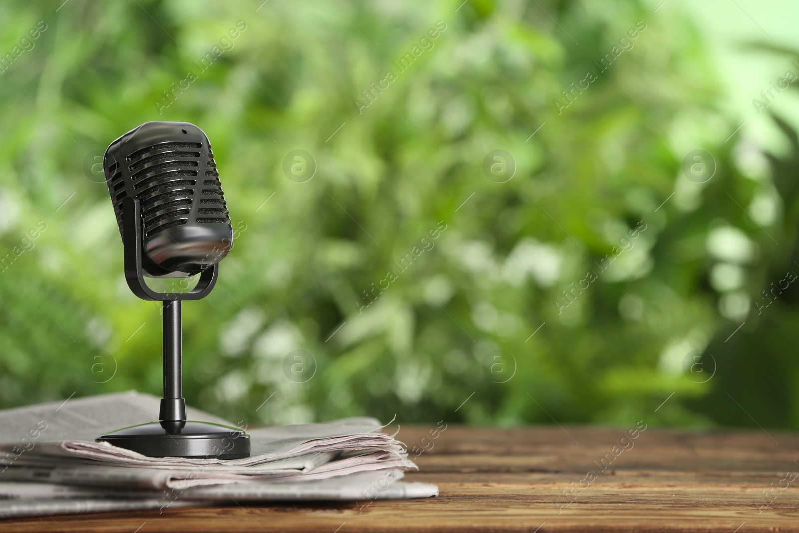 Photo of Newspapers and vintage microphone on wooden table against blurred green background, space for text. Journalist's work