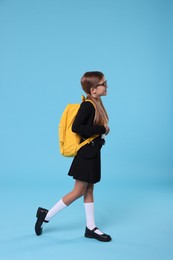 Photo of Happy schoolgirl with backpack on light blue background