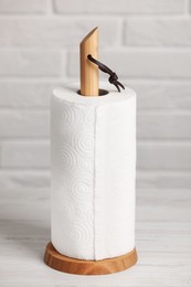 Photo of Holder with roll of paper towels on white wooden table near brick wall
