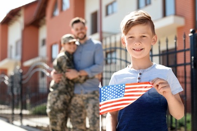 Photo of Little boy with American flag and his parents in military uniform outdoors