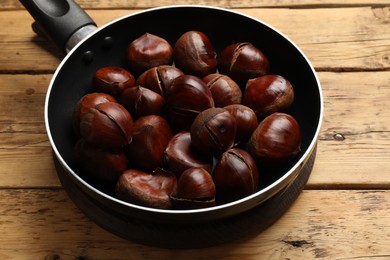 Photo of Fresh edible sweet chestnuts in frying pan on wooden table