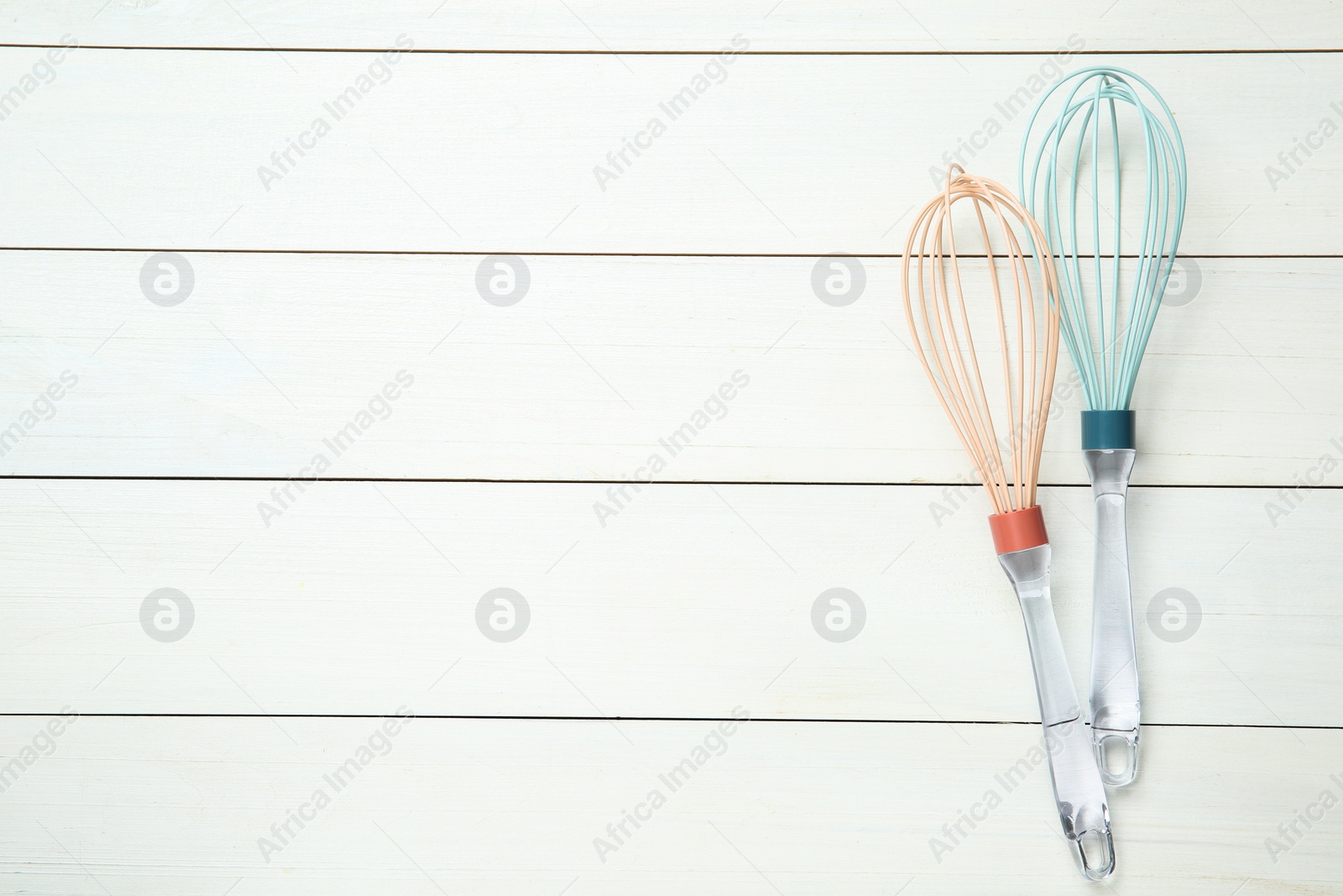 Photo of Two whisks on white wooden table, top view. Space for text