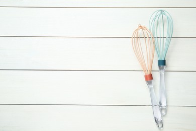 Photo of Two whisks on white wooden table, top view. Space for text