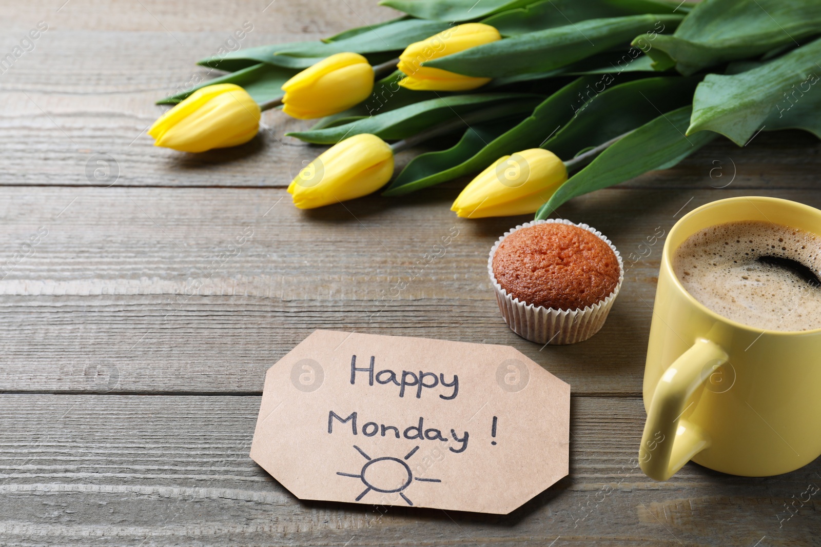 Photo of Happy Monday message, aromatic coffee, cupcake and tulips on wooden table