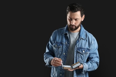 Man taking cigarette from case on black background, space for text