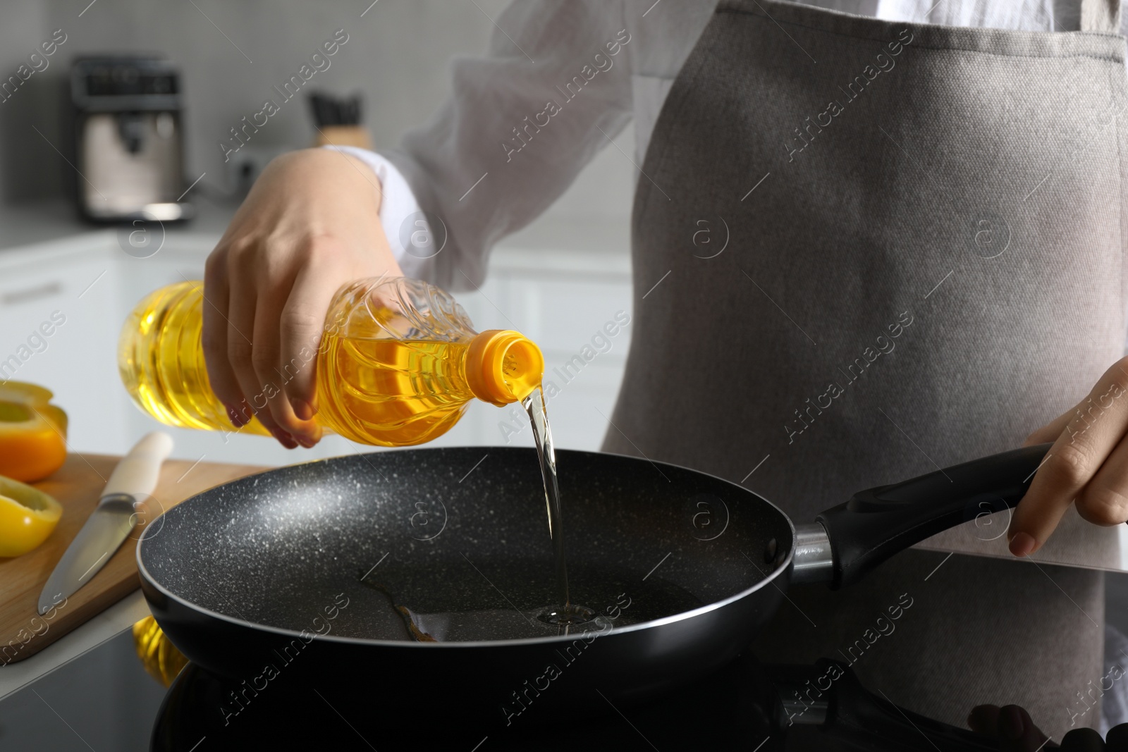 Photo of Woman pouring cooking oil from bottle into frying pan on stove, closeup