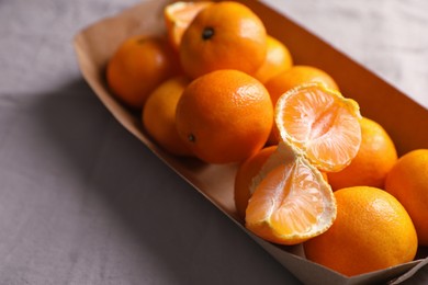 Paper box with fresh ripe tangerines on beige cloth, closeup