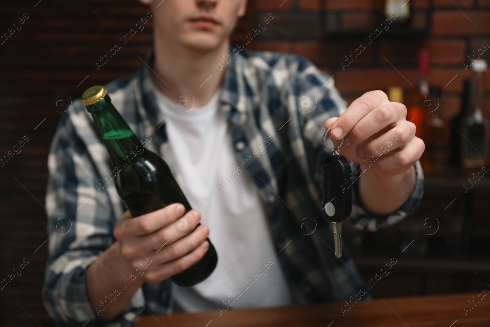 Photo of Man with bottle of beer and car keys in bar, closeup. Don't drink and drive concept