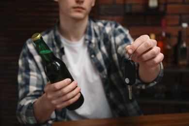 Photo of Man with bottle of beer and car keys in bar, closeup. Don't drink and drive concept