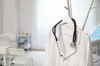 Photo of White doctor's gown and stethoscope on rack in clinic, closeup. Space for text