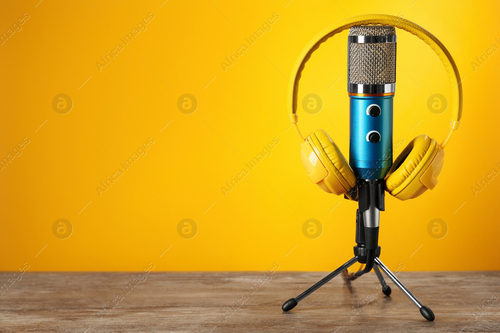 Photo of Microphone and modern headphones on wooden table against orange background, space for text