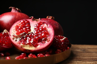 Photo of Tray with ripe pomegranates on table against black background, space for text