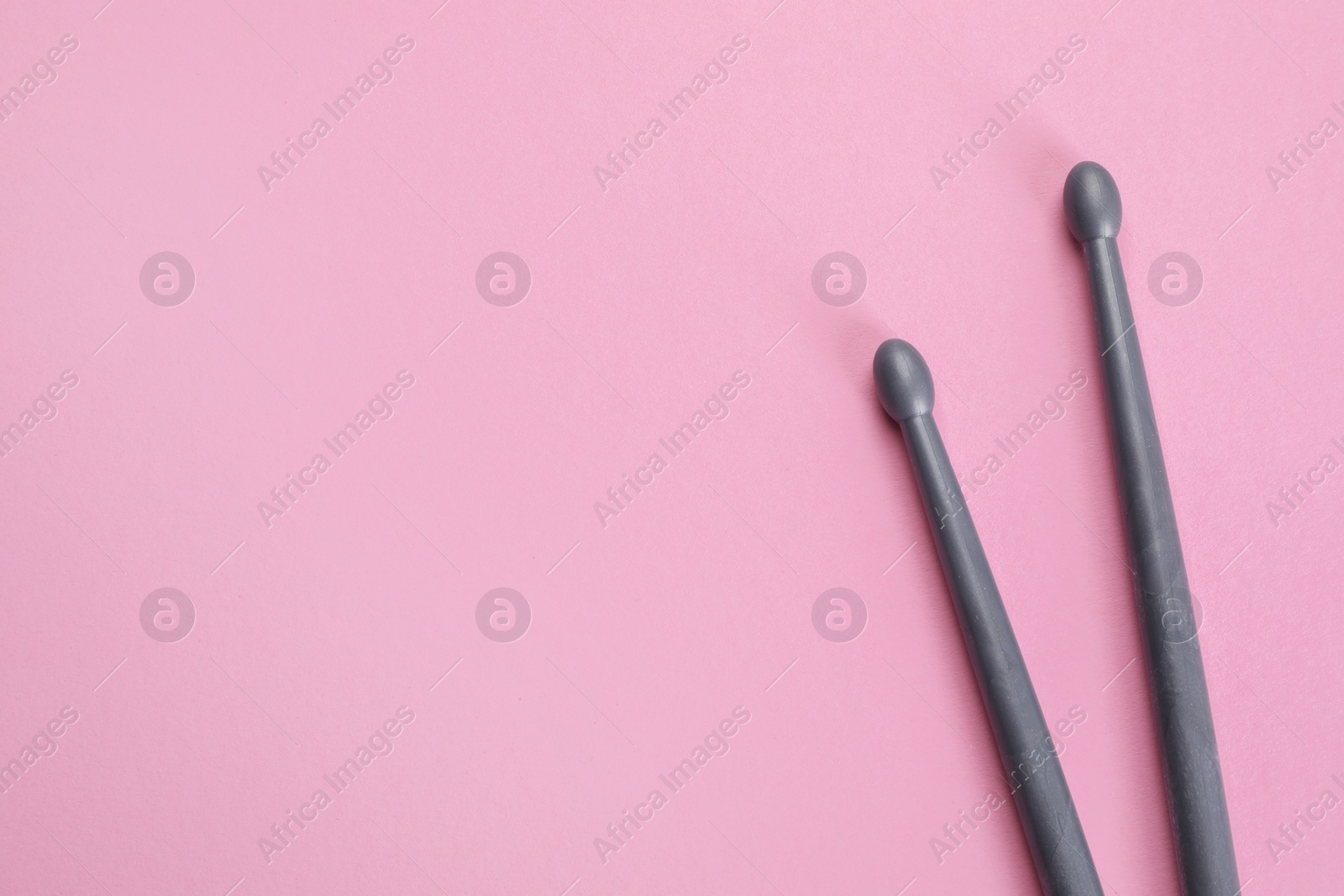 Photo of Two grey drumsticks on pink background, top view. Space for text